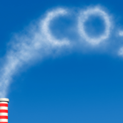 A factory smokestack emitting a cloud shaped as 'CO₂,' symbolizing carbon dioxide emissions and environmental impact.