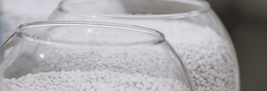 Close-up image of white plastic pellets in glass containers, showcasing raw material used in polymer processing and extrusion.