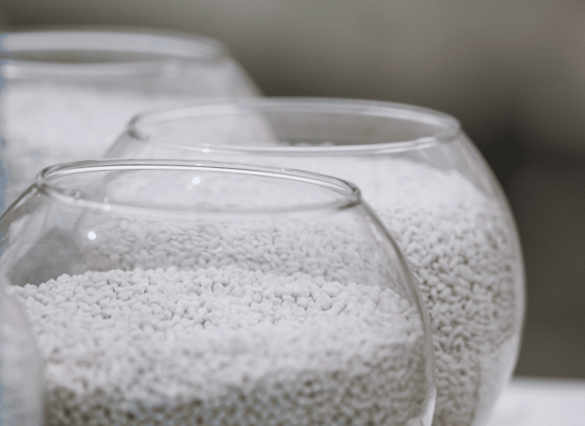 Close-up image of white plastic pellets in glass containers, showcasing raw material used in polymer processing and extrusion.