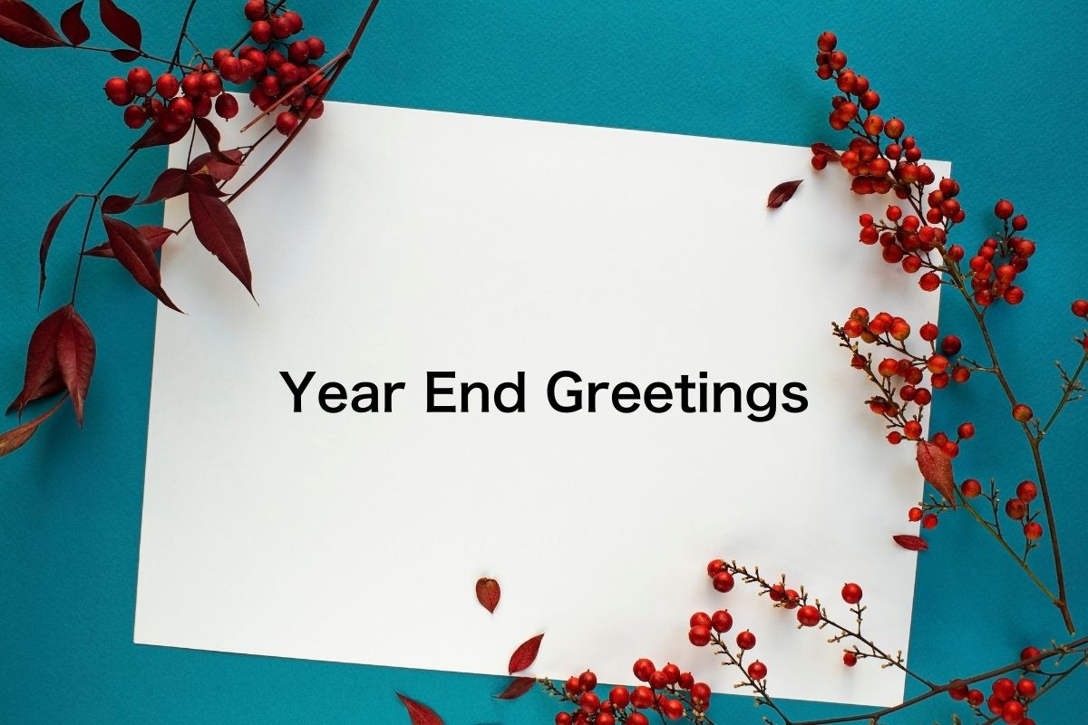 A festive year-end greeting card with the words 'Year End Greetings' on a white sheet, surrounded by vibrant red berries and autumn leaves on a teal background.