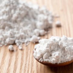 Close-up image of fine biomass raw material powder on a wooden surface, with a spoon holding a portion of the material, representing biomass raw material compounds for sustainable processing.