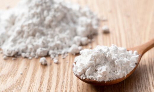 Close-up image of fine biomass raw material powder on a wooden surface, with a spoon holding a portion of the material, representing biomass raw material compounds for sustainable processing.