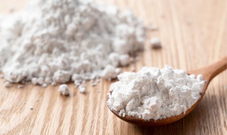 Close-up image of fine biomass raw material powder on a wooden surface, with a spoon holding a portion of the material, representing biomass raw material compounds for sustainable processing.