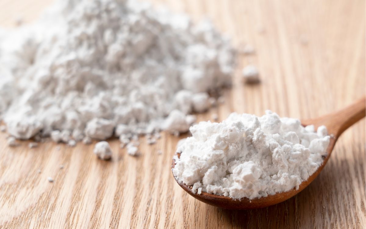 Close-up image of fine biomass raw material powder on a wooden surface, with a spoon holding a portion of the material, representing biomass raw material compounds for sustainable processing.