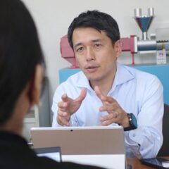 Masato Ito, CEO of CTE, engaging in conversation about extrusion technology with a model of the HTM Twin Screw Extruder visible behind him.