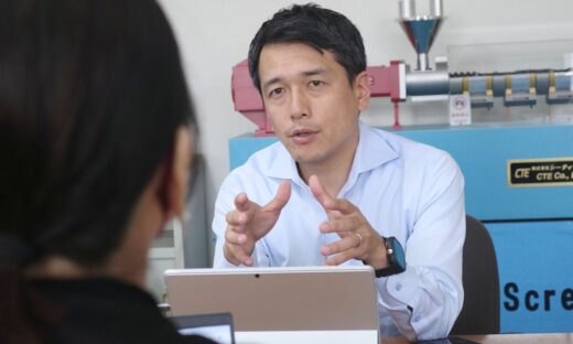 Masato Ito, CEO of CTE, engaging in conversation about extrusion technology with a model of the HTM Twin Screw Extruder visible behind him.