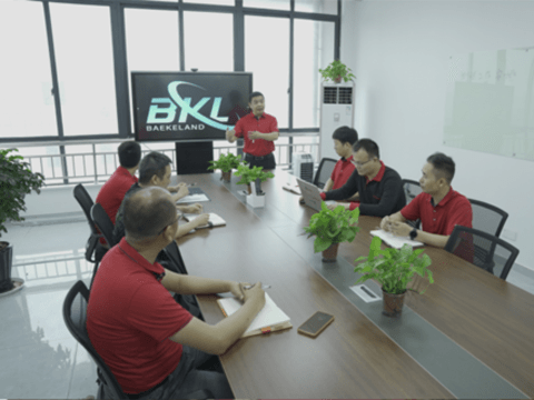 A team of Baekeland employees in a conference room during a business meeting, with a presentation displayed on a large screen showing the Baekeland (BKL) logo. Baekeland is CTE's conical extruder partner in China.