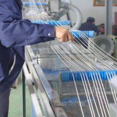 Worker adjusting extruded strands passing through a cooling water tank during the extrusion process, ensuring quality control and proper cooling for optimal product performance.