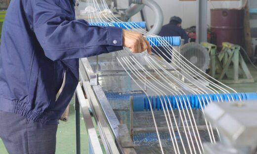 Worker adjusting extruded strands passing through a cooling water tank during the extrusion process, ensuring quality control and proper cooling for optimal product performance.