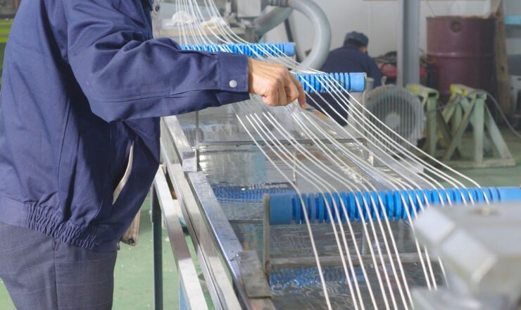 Worker adjusting extruded strands passing through a cooling water tank during the extrusion process, ensuring quality control and proper cooling for optimal product performance.