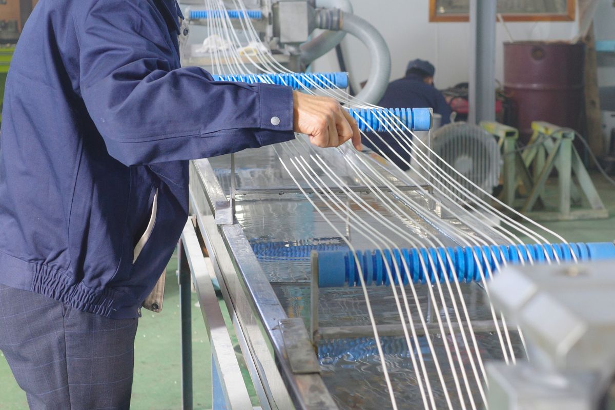 Worker adjusting extruded strands passing through a cooling water tank during the extrusion process, ensuring quality control and proper cooling for optimal product performance.