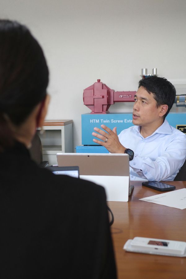 Masato Ito, CEO of CTE, explaining the benefits of the HTM Twin Screw Extruder during a meeting, with a clear view of the machine model in the background.