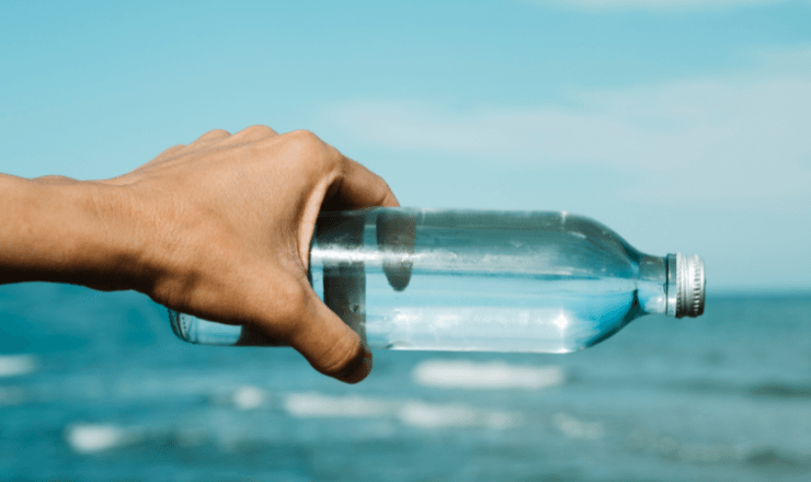 Hand holding a clear recycled plastic bottle against a blue sky backdrop, symbolizing environmental sustainability and the recycling process.