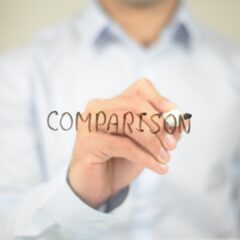 「COMPARISON」と書かれた透明なボードにマーカーで文字を書くビジネスマンの手元。比較や分析をテーマにしたコンセプトイメージ。